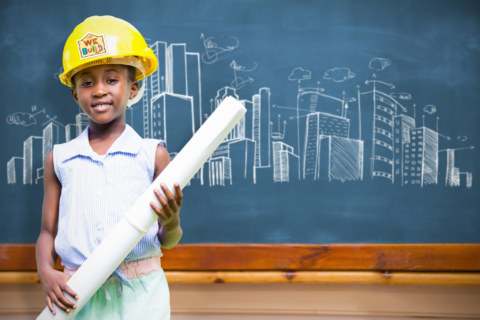 Little,Girl,Wearing,Yellow,Helmet,And,Construction,Plan,Against,Blackboard